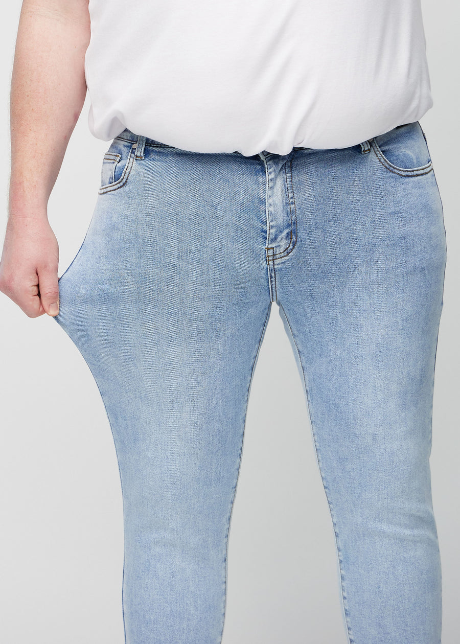 Ein Plus-Size-Model dehnt die Jeans am Oberschenkel, um den Stretch des Materials zu zeigen.