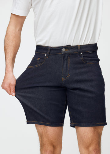 model dehnt dunkelblaue denim shorts für herren in der farbe midnights am oberschenkel, um den stretch des materials zu zeigen.