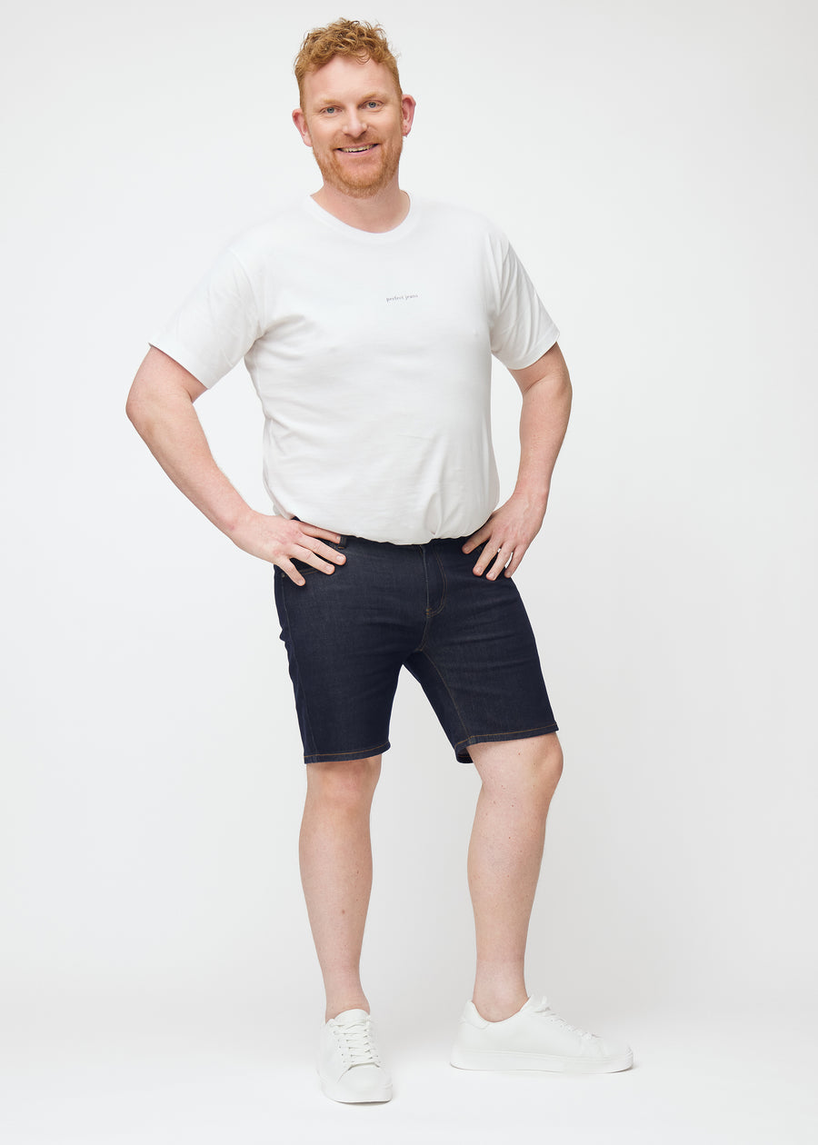 Ganzkörperbild eines Plus-Size-Models in tief dunkelblauen Denim-Shorts für Herren in der Farbe Midnights mit Slim-Passform.