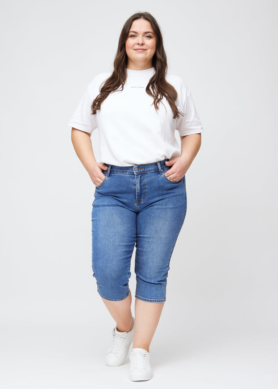 Fuldt billede af plus-size model i blå denim slim capris.