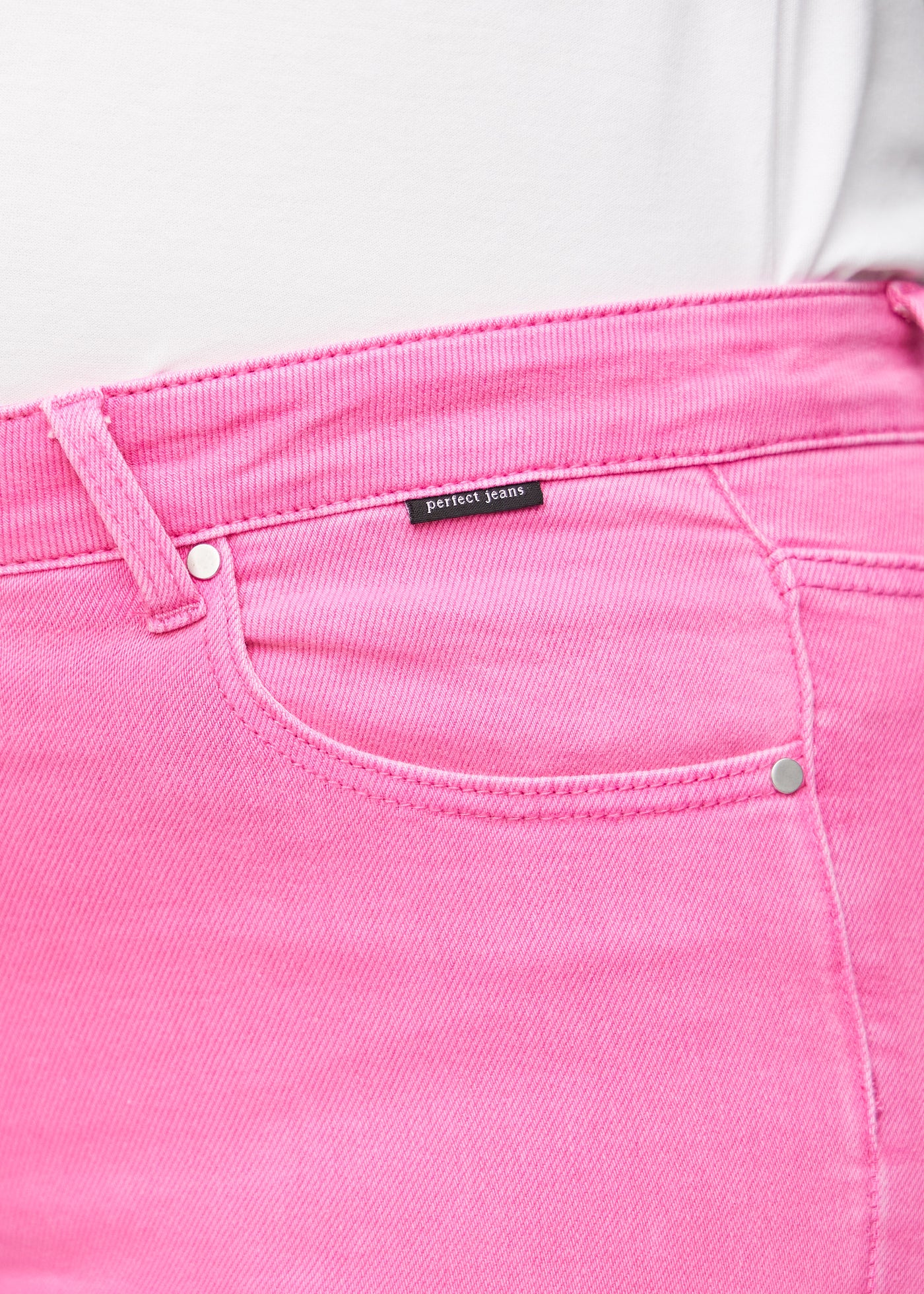 Detaljebillede af forlommen på de lyserøde slim capris i farven Flamingos – logo og snit fremhævet på plus-size model.