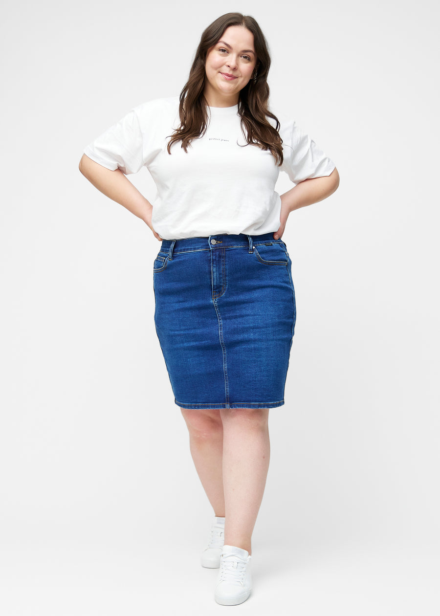 Plus-size model viser mørkeblå, tætsiddende og knælang denimnederdel i bevægelse og strækker materialet.