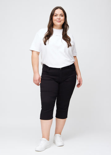 Plus-size model går ind i billedet, strækker i sine sorte slim capris, drejer rundt for at vise dem frem og forlader derefter billedet.