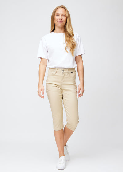  Model træder ind i billedet, strækker i sine beige slim capris, viser dem frem ved at dreje rundt, og går derefter ud af billedet igen.